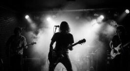 Drei Musiker spielen ein Clubkonzert auf einer nebligen, dunkel beleuchteten Bühne
